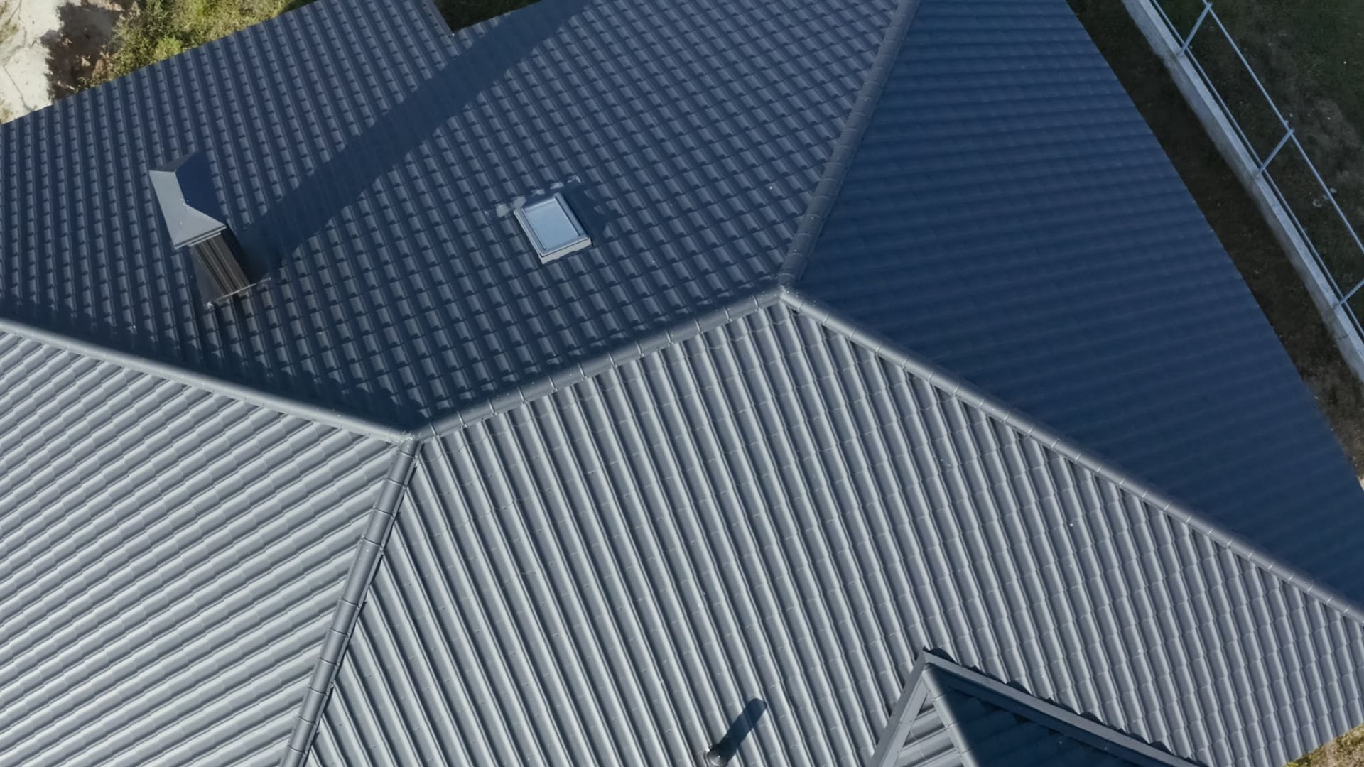 A close-up aerial shot of a house with a blue roof, showcasing the texture of the metal sheets and the roof's geometric design.
