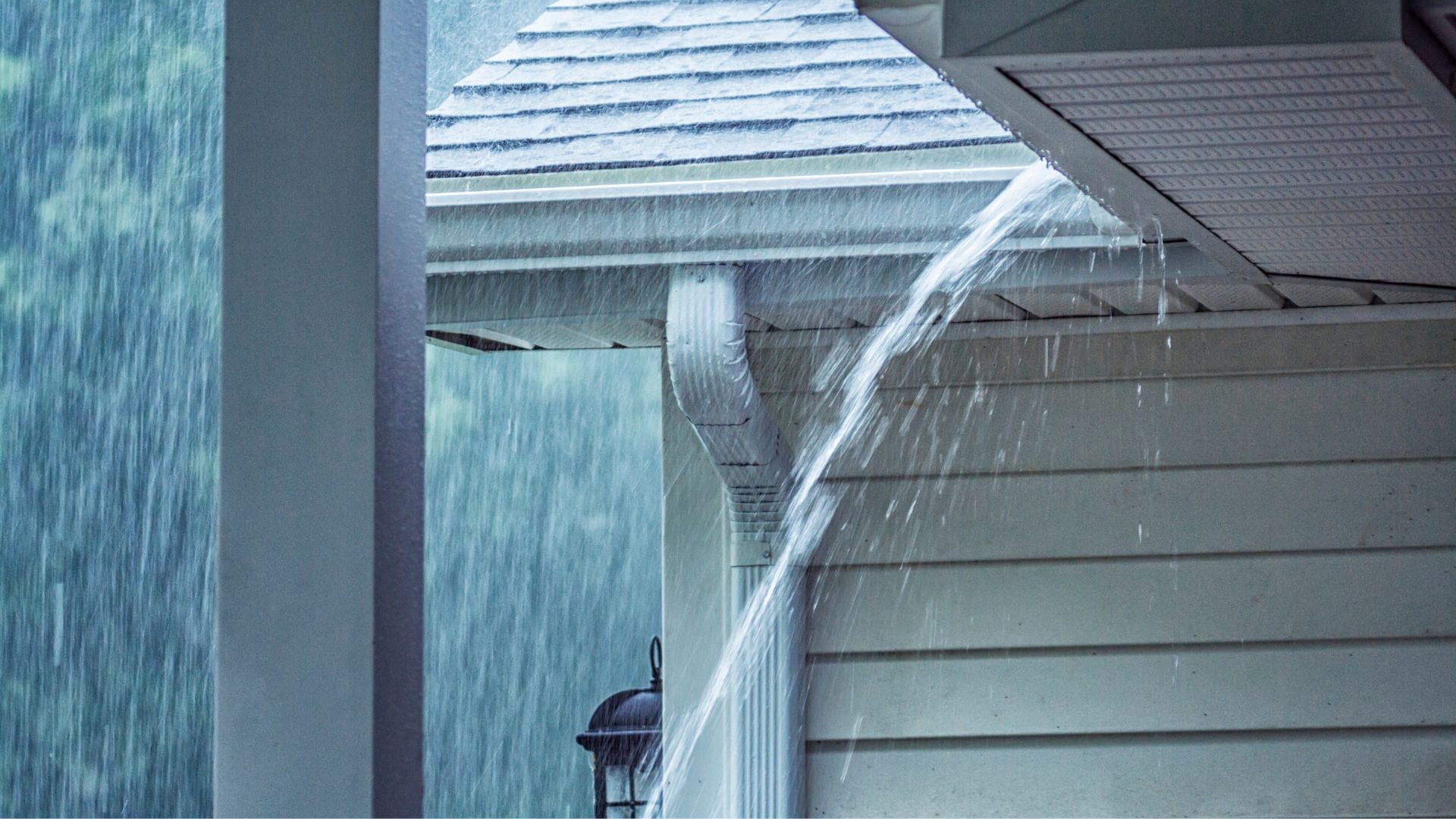 A house gutter system unable to handle the heavy rain, causing water to overflow and spill over the edge, creating a cascading effect.