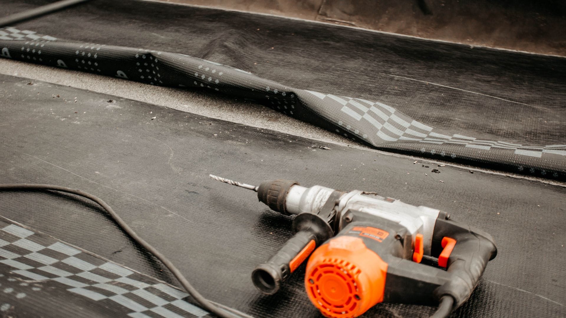 A close-up of a partially installed roofing membrane with a power drill resting on top, showing an ongoing roofing maintenance.