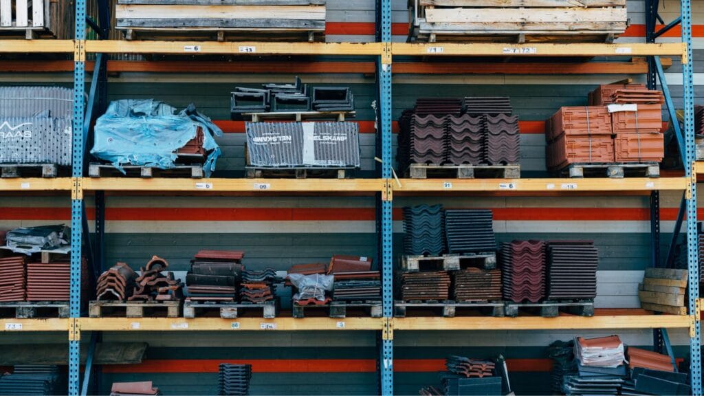 A warehouse storage rack filled with various roofing materials, including tiles and sheets, neatly stacked on wooden pallets.