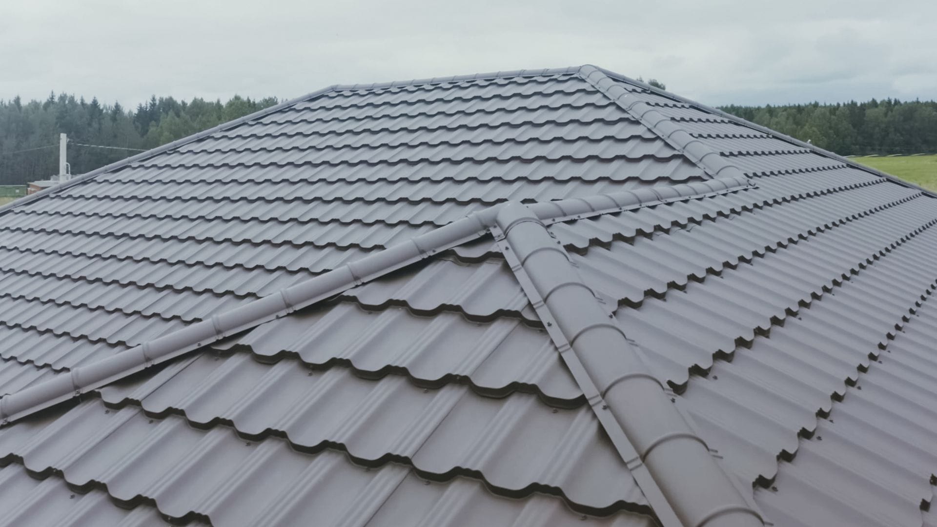 A house with a modern grey metal tile roof, featuring multiple ridges and slopes.
