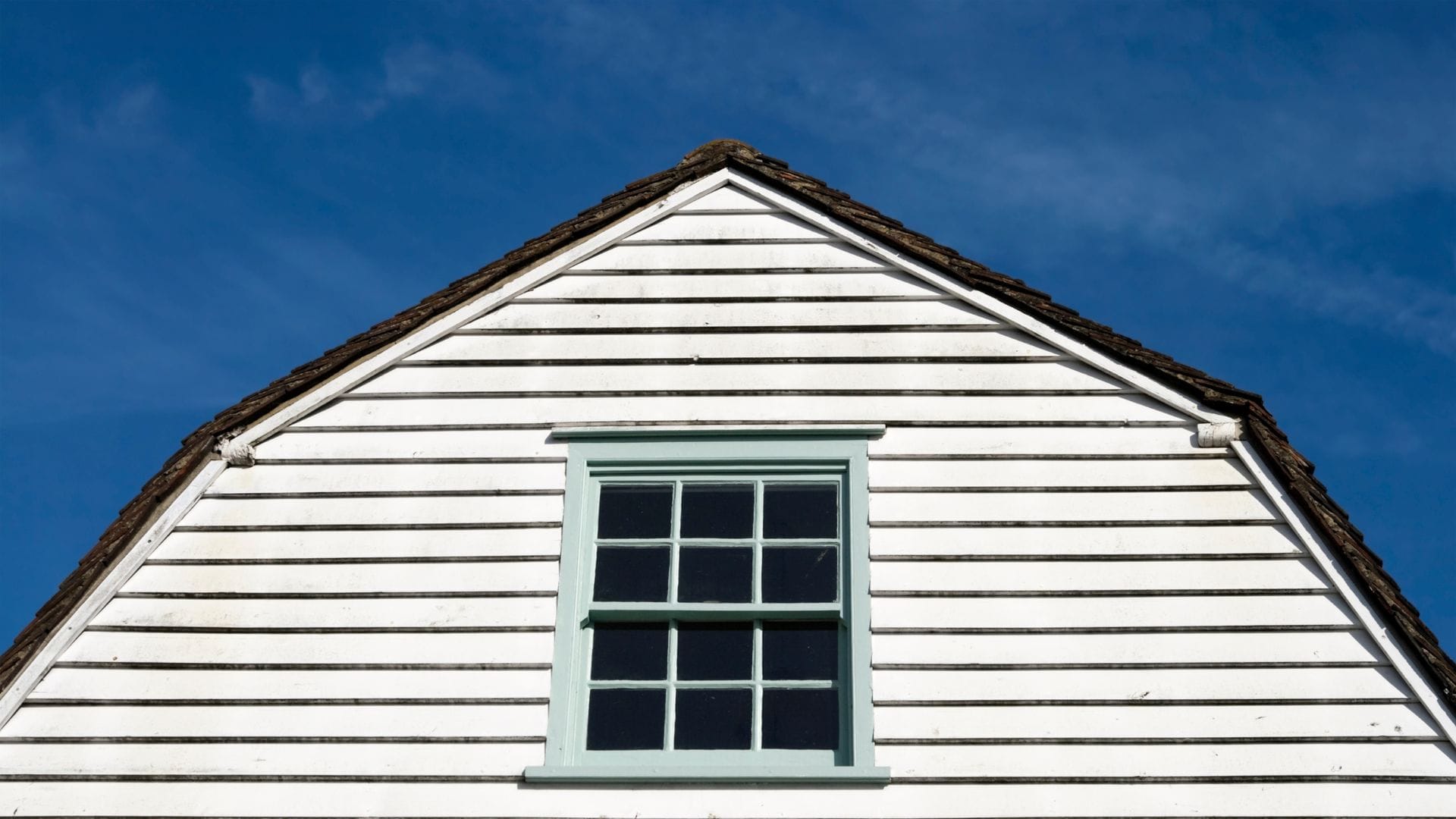 A traditional white wooden house with a pitched roof covered in aged wooden shingles.
