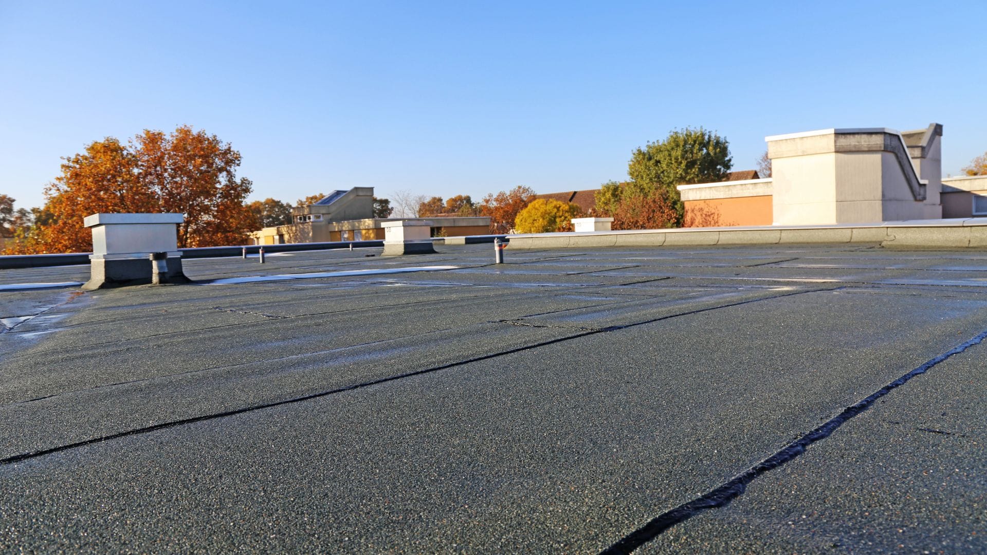 Flat commercial roof with visible seams and rooftop structures under a clear blue sky.