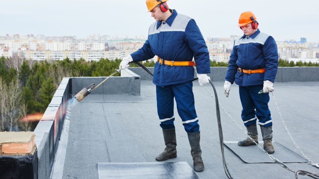 Two workers applying heat to seal a flat roof with waterproof material.